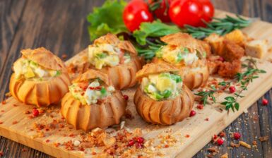 Choux-uri sărate umplute cu salată de legume cu maioneză pe un platou de lemn, cu roșii și salată verde