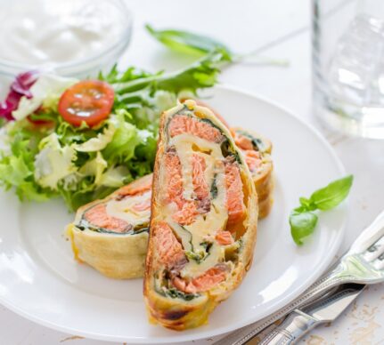 Două porții de ștrudel cu somon, spanac și cașcaval pe o farfurie cu salată