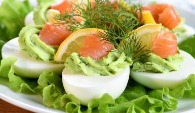 Ouă umplute cu avocado și somon afumat, decorate cu mărar și așezate pe frunze de salată verde
