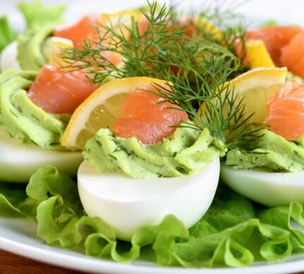 Ouă umplute cu avocado și somon afumat, decorate cu mărar și așezate pe frunze de salată verde