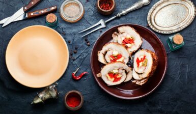 Patru porții de Ruladă de porc cu gogoșari murați, măsline verzi și cașcaval pe un platou, tacâmuri, condimente, o farfurie și un platou