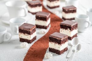 Prăjitură cu blat de cacao, cremă de vanilie și glazură subțire de ciocolată porționată