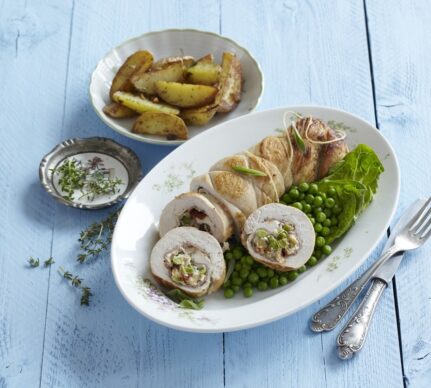 Ruladă de curcan cu brânză cremoasă, mazăre și roșii uscate porționată pe un platou cu mazăre, alături de un bol cu cartofi și unul cu sos