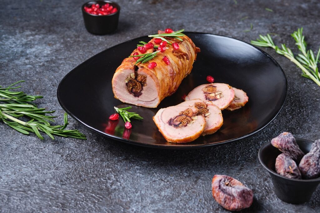 Ruladă de porc cu smochine și nuci, în felii de bacon porționată pe o farfurie neagră