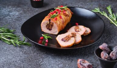 Ruladă de porc cu smochine și nuci, în felii de bacon porționată pe o farfurie neagră