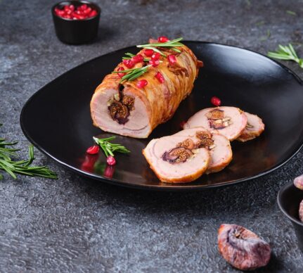 Ruladă de porc cu smochine și nuci, în felii de bacon porționată pe o farfurie neagră