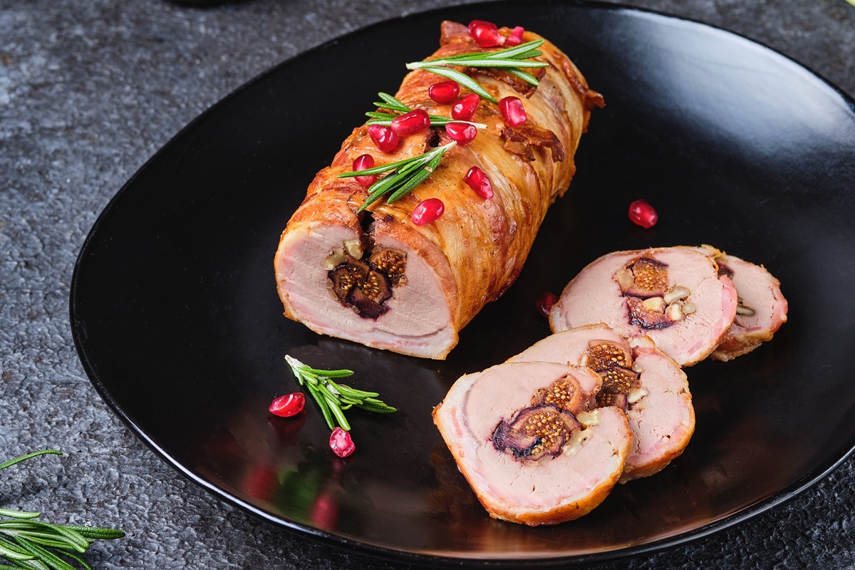 Ruladă de porc cu smochine și nuci, în felii de bacon porționată pe o farfurie neagră