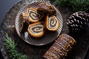 Ruladă din aluat de cozonac cu nucă și cacao, glazurată cu ciocolată porționată pe farfurie și o bucată neporționată