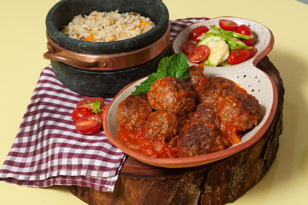 Chiftele în sos de ceapă caramelizată cu bulion, alături de un bol cu orez și unul cu salată