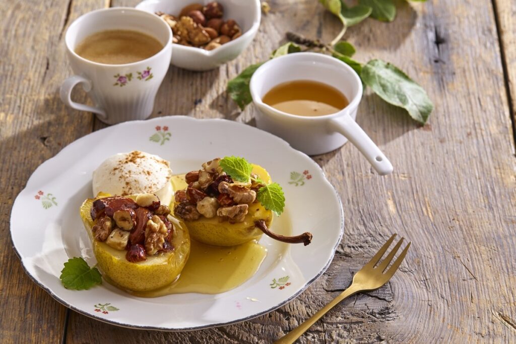 Jumătăți de pere cu miere, nuci și alune pe două farfurii cu furculițe și un bol cu miere