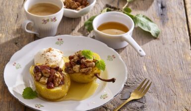 Jumătăți de pere cu miere, nuci și alune pe două farfurii cu furculițe și un bol cu miere