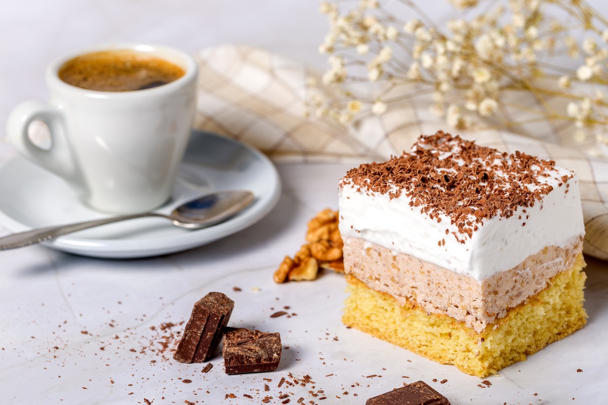 Porție de prăjitură cu cremă de nuci și frișcă lângă o ceașcă de cafea cu linguriță