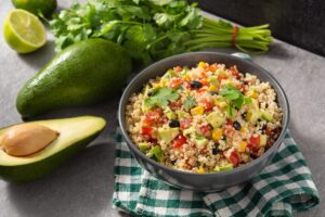 Salată cu quinoa, legume mexicane și avocado în bol, alături de un avocado întreg,, unul jumătate și pătrunjel verde