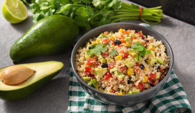 Salată cu quinoa, legume mexicane și avocado în bol, alături de un avocado întreg,, unul jumătate și pătrunjel verde