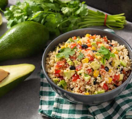 Salată cu quinoa, legume mexicane și avocado în bol, alături de un avocado întreg,, unul jumătate și pătrunjel verde