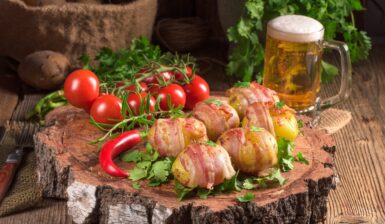 Cartofi înveliți în bacon pe un un pat de frunze de pătrunjel, așezat pe un tocător de lemn