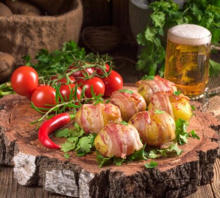 Cartofi înveliți în bacon pe un un pat de frunze de pătrunjel, așezat pe un tocător de lemn