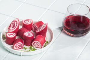 Clătite cu sfeclă roșie în aluat și cremă de brânză porționate pe o farfurie și un pahar cu suc de sfeclă