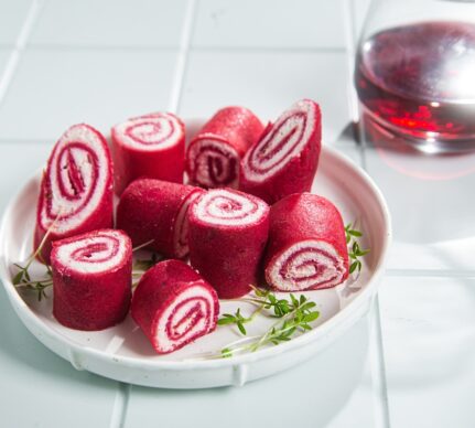 Clătite cu sfeclă și cremă de brânză porționate pe o farfurie și un pahar cu suc de sfeclă