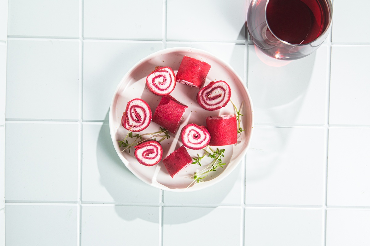 Clătite cu sfeclă roșie în aluat și cremă de brânză porționate pe o farfurie și un pahar cu suc de sfeclă