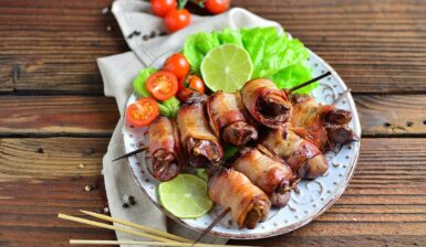 Ficăței de pui înfășurați în bacon pe bețe de frigărui și salată de legume pe o farfurie