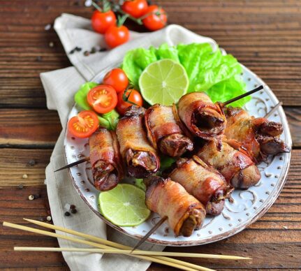 Ficăței de pui înfășurați în bacon pe bețe de frigărui și salată de legume pe o farfurie