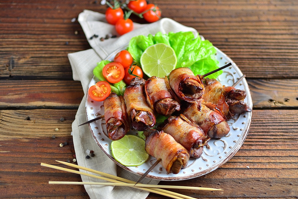 Ficăței de pui înfășurați în bacon pe bețe de frigărui și salată de legume pe o farfurie