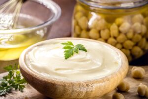 Maioneză vegetală din aquafaba în bol, un borcan cu năut în saramură și un bol cu aquafaba și un tel