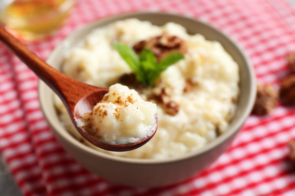 Orez cremos cu lapte de cocos în bol cu linguriță, decorat cu nuci și mentă