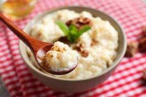 Orez cremos cu lapte de cocos în bol cu linguriță, decorat cu nuci și mentă