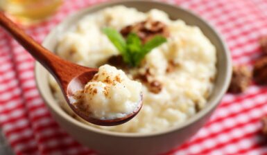 Orez cremos cu lapte de cocos în bol cu linguriță, decorat cu nuci și mentă