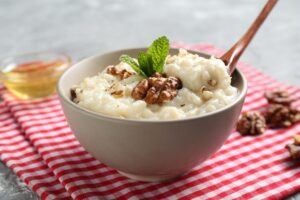 Orez cremos cu lapte de cocos în bol cu linguriță, decorat cu nuci și mentă