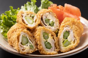 Cordon bleu cu sparanghel în interior porționat, alături de roșii feliate și salată verde