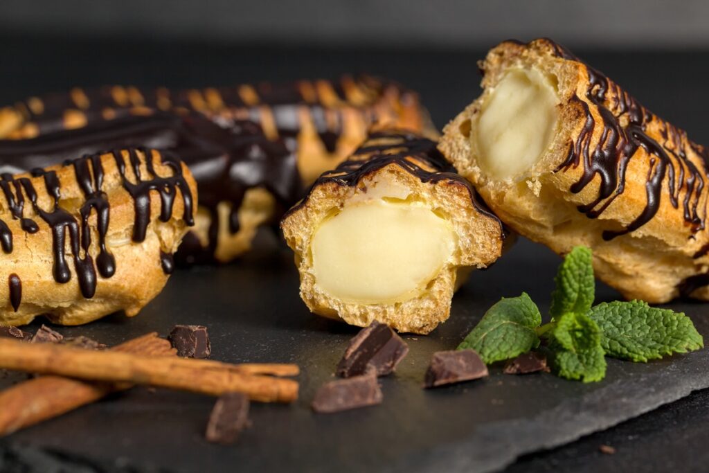 Eclere cu cremă de vanilie și glazură de ciocolată, unul secționat