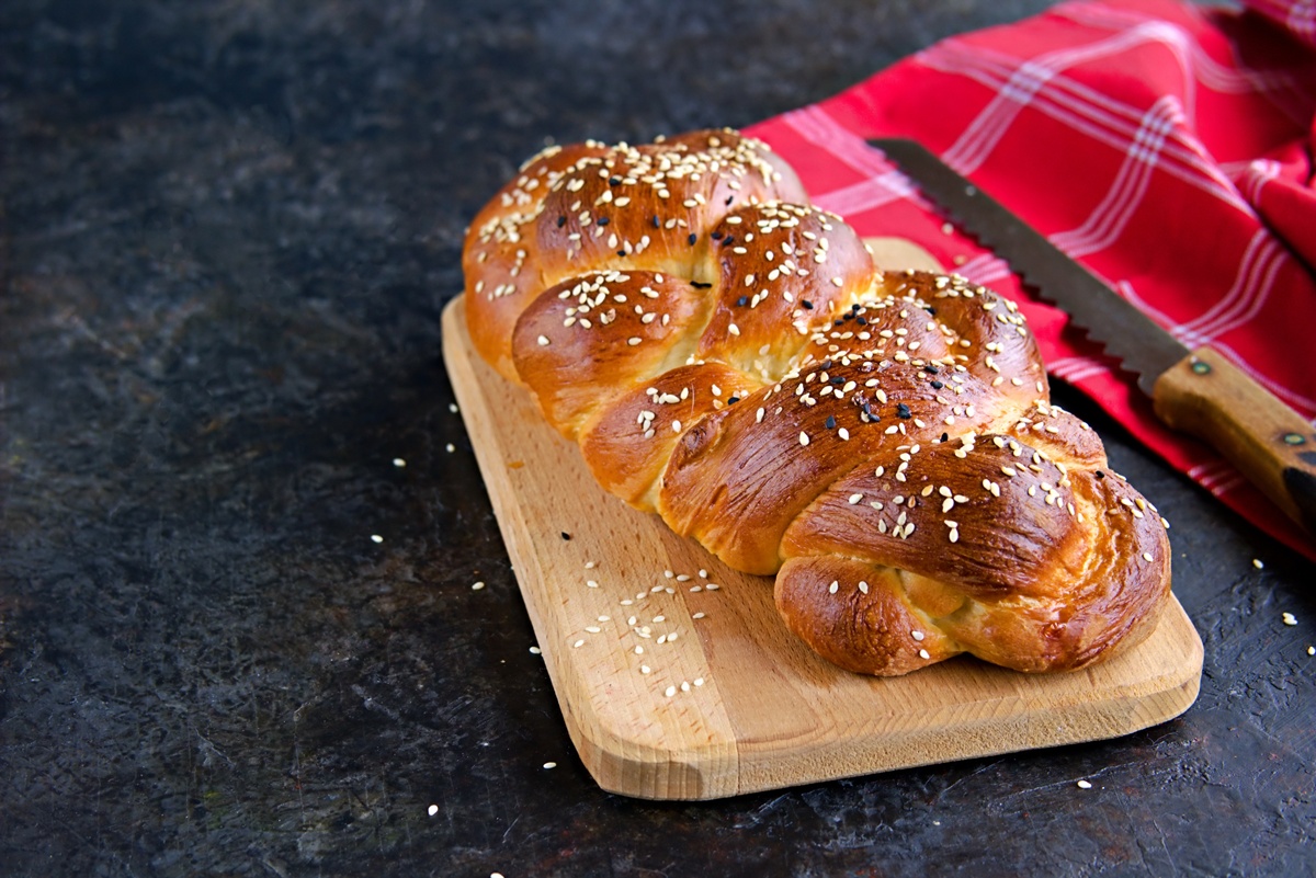 Pâine albă împletită, decorată cu semințe de susan pe un tocător de lemn