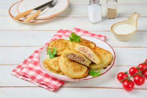 Plăcinte de cartofi cu carne tocată pe o farfurie, una secționată