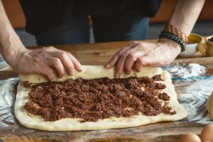 Două mâini rulând aluatul de cozonac cu umplutură de halva și nuci