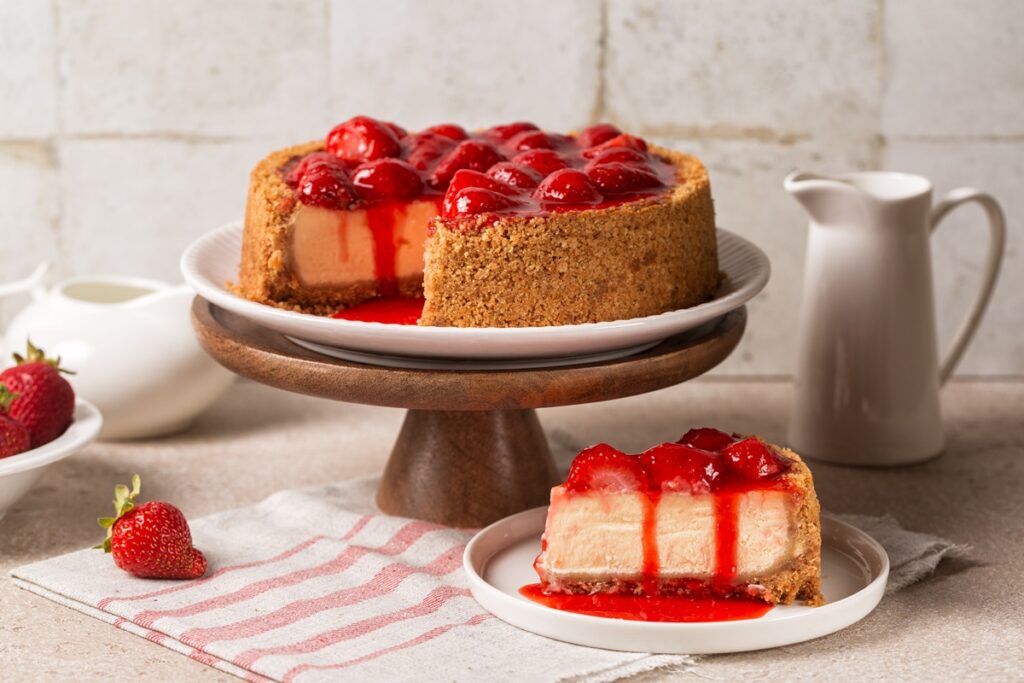 Cheesecake cu crustă crocantă de biscuiți și căpșuni porționat pe farfurie și pe platou