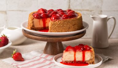 Cheesecake cu crustă crocantă de biscuiți și căpșuni porționat pe farfurie și pe platou