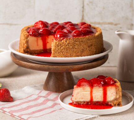 Cheesecake cu crustă crocantă de biscuiți și căpșuni porționat pe farfurie și pe platou