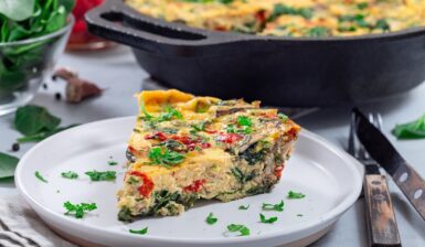 Porție de frittata cu spanac și ardei copți pe farfurie, alături de vasul cu frittata