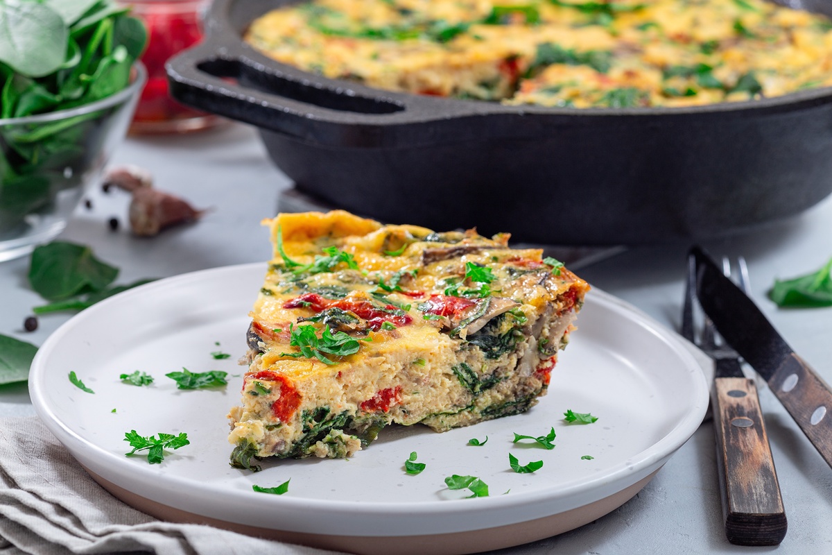 Porție de frittata cu spanac și ardei copți pe farfurie, alături de vasul cu frittata