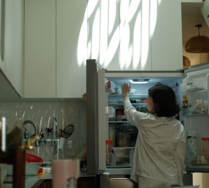 Femeie deschizând un frigider pentru a-și răspunde la întrebarea ”De ce unele alimente au un gust mai bun a doua zi”.