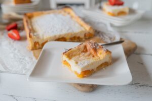 Porție de tartă cu caise și cremă de vanilie pe o farfurie și tarta secționată pe platou