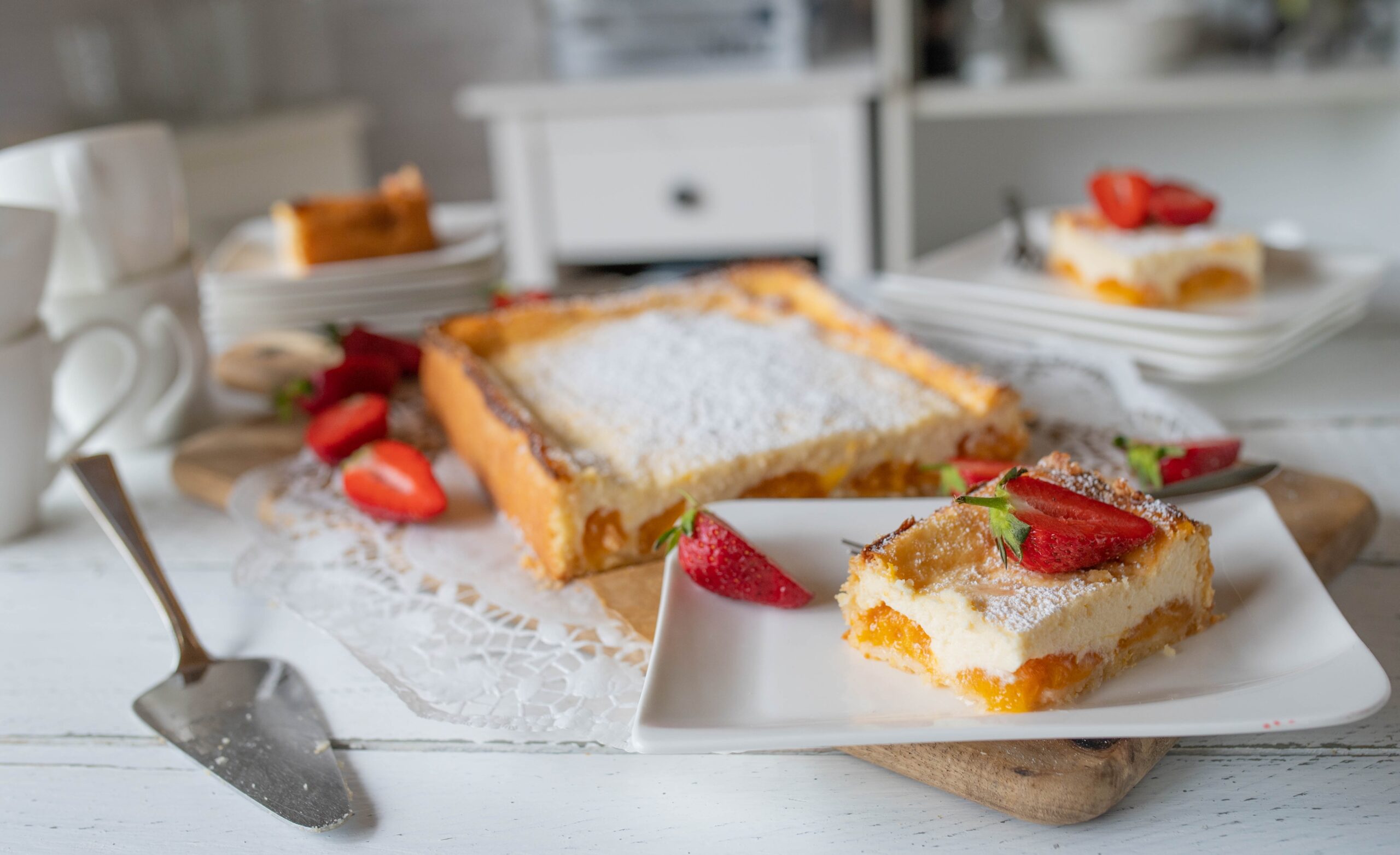 Porție de tartă cu caise și cremă de vanilie pe o farfurie și tarta secționată pe platou